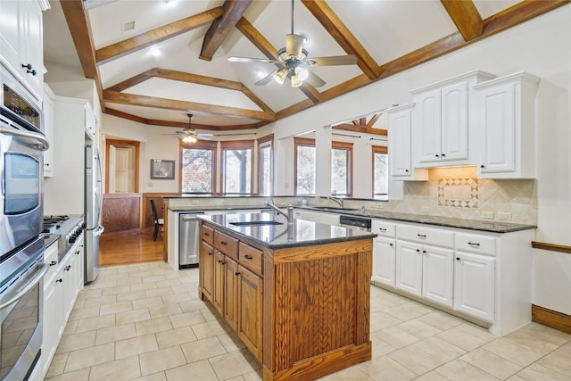 kitchen featuring appliances with stainless steel finishes, dark stone counters, a kitchen island with sink, sink, and white cabinets