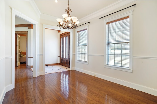 foyer entrance with hardwood / wood-style floors, a wealth of natural light, crown molding, and a notable chandelier