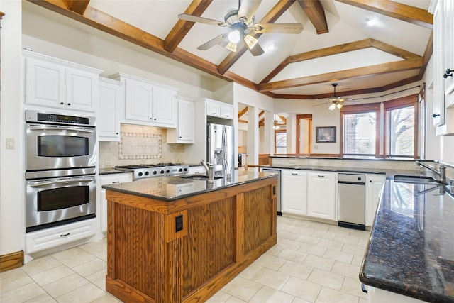 kitchen featuring appliances with stainless steel finishes, dark stone counters, sink, a center island with sink, and white cabinetry