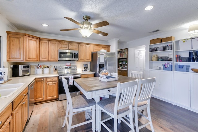 kitchen with ceiling fan, stainless steel appliances, light hardwood / wood-style flooring, crown molding, and a textured ceiling