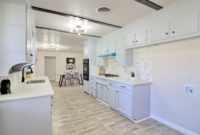 kitchen with stainless steel gas cooktop, sink, black oven, decorative backsplash, and white cabinets