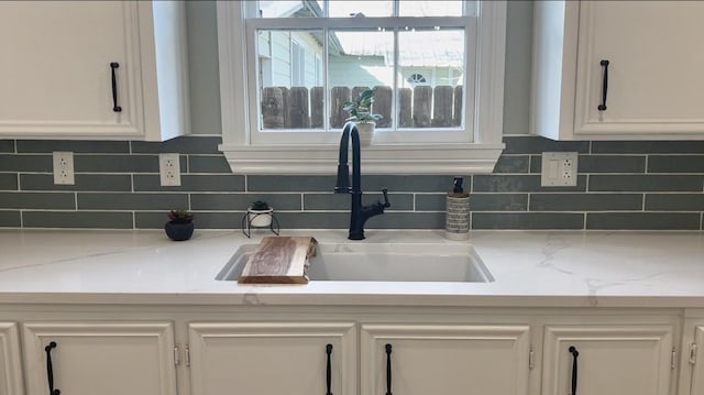 interior details featuring light stone counters, white cabinetry, sink, and tasteful backsplash