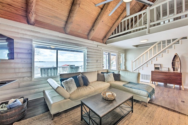 living room featuring beamed ceiling, rustic walls, ceiling fan, and wooden ceiling