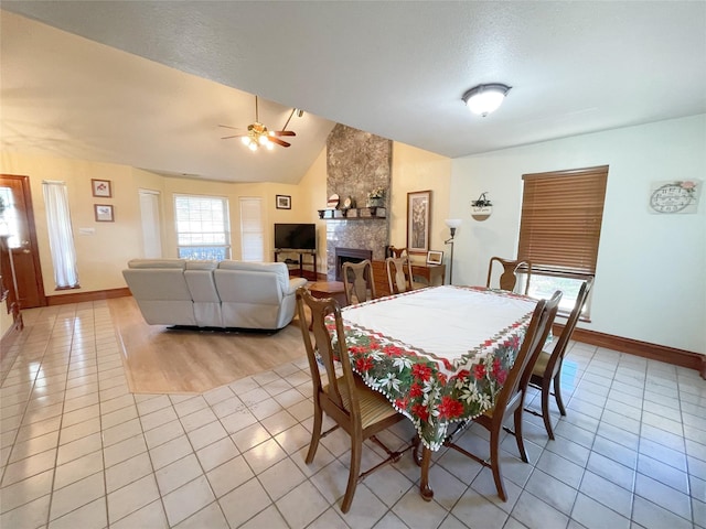 dining area featuring light tile patterned floors, ceiling fan, a large fireplace, a textured ceiling, and vaulted ceiling