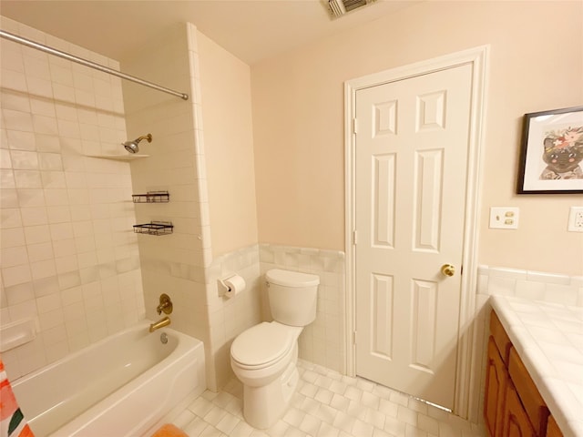 full bathroom with tiled shower / bath, tile walls, tile patterned flooring, vanity, and toilet