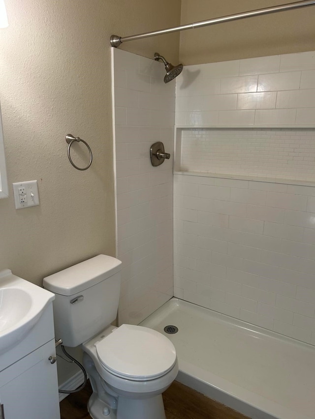 bathroom featuring a tile shower, vanity, toilet, and wood-type flooring