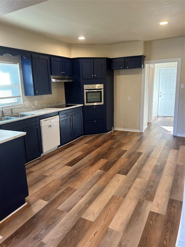 kitchen with stainless steel oven, sink, blue cabinets, hardwood / wood-style floors, and white dishwasher