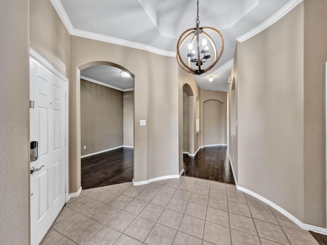 tiled foyer entrance with ornamental molding, a tray ceiling, and an inviting chandelier