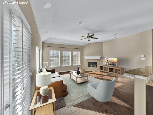 tiled living room with ceiling fan and a fireplace