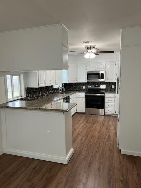 kitchen with appliances with stainless steel finishes, white cabinetry, dark hardwood / wood-style flooring, kitchen peninsula, and dark stone counters