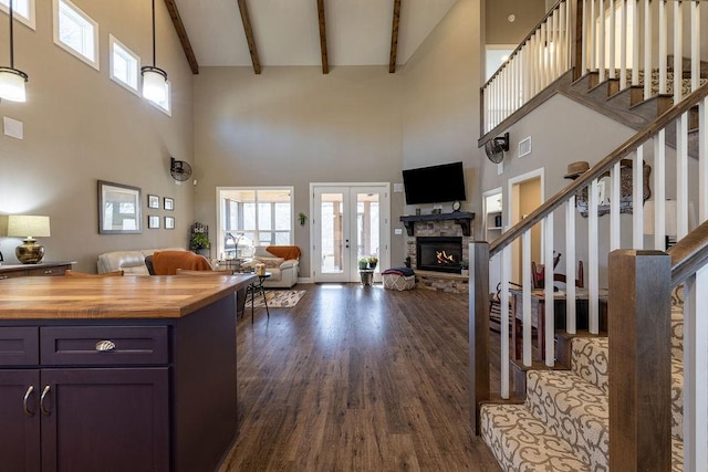 interior space featuring french doors, dark hardwood / wood-style flooring, beamed ceiling, a towering ceiling, and a fireplace