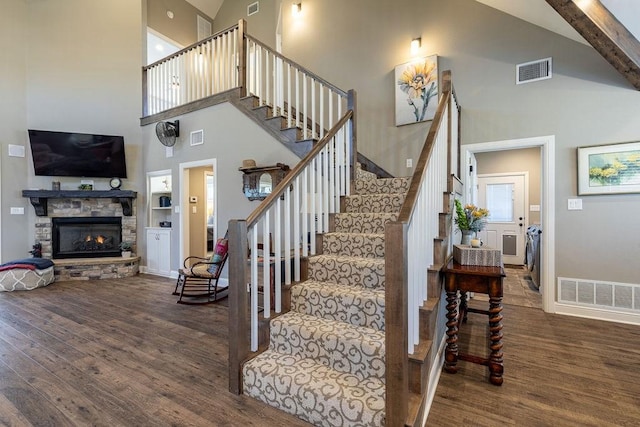 stairs with a stone fireplace, hardwood / wood-style floors, and a towering ceiling