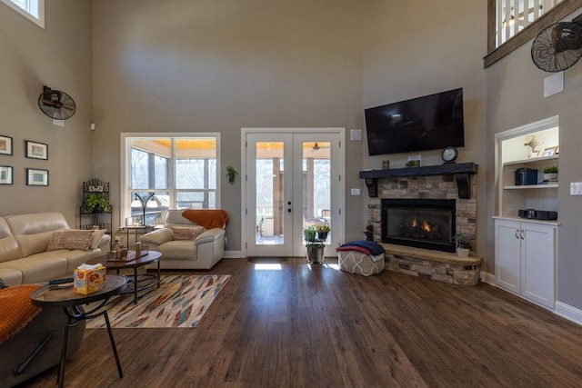 living room with built in shelves, a fireplace, a towering ceiling, and dark wood-type flooring