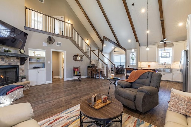 living room with dark hardwood / wood-style flooring, high vaulted ceiling, a stone fireplace, and sink