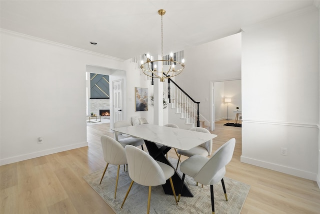 dining area featuring an inviting chandelier, a fireplace, crown molding, and light hardwood / wood-style flooring