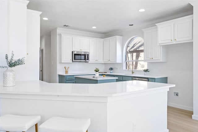 kitchen featuring white cabinetry, a breakfast bar area, appliances with stainless steel finishes, decorative backsplash, and light hardwood / wood-style flooring