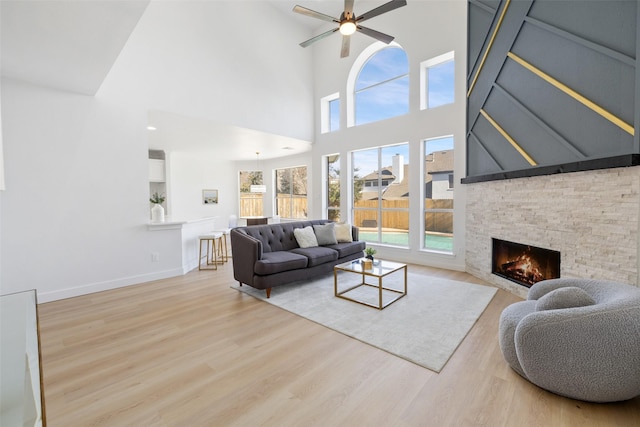 living room featuring ceiling fan, a wealth of natural light, a stone fireplace, and light wood-type flooring