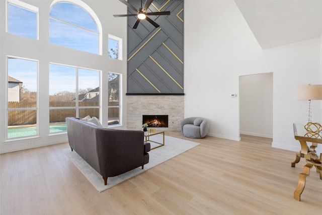 living room featuring ceiling fan, a towering ceiling, light hardwood / wood-style flooring, and a stone fireplace