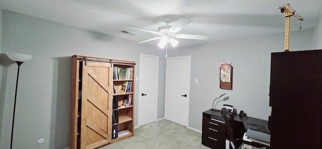 carpeted office space featuring a barn door and ceiling fan