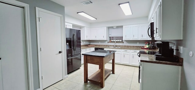 kitchen with white cabinets, light tile patterned floors, black fridge, and sink