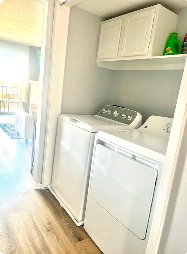 laundry area with cabinets, light wood-type flooring, and washer and clothes dryer