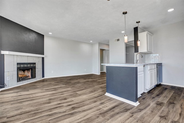 kitchen featuring white cabinetry, backsplash, a tiled fireplace, hanging light fixtures, and dark wood-type flooring