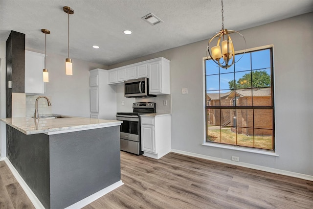 kitchen featuring sink, white cabinetry, stainless steel appliances, decorative light fixtures, and kitchen peninsula