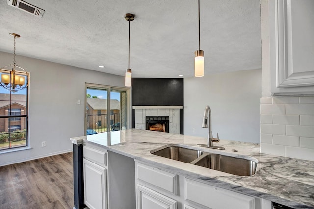 kitchen with white cabinetry, sink, decorative light fixtures, and light stone countertops