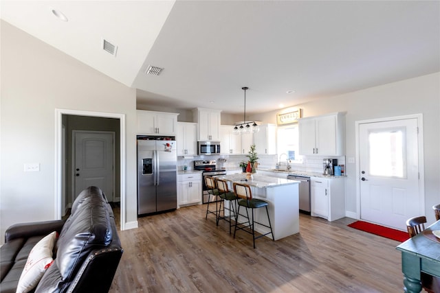 kitchen featuring tasteful backsplash, light stone counters, stainless steel appliances, a center island, and hanging light fixtures