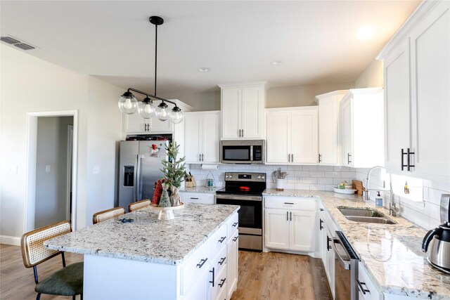 kitchen with stainless steel appliances, sink, decorative light fixtures, a center island, and white cabinetry