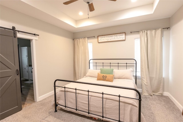 bedroom with ceiling fan, a barn door, light carpet, and a tray ceiling