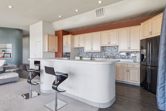 kitchen with stainless steel oven, black refrigerator, an island with sink, tasteful backsplash, and a kitchen bar