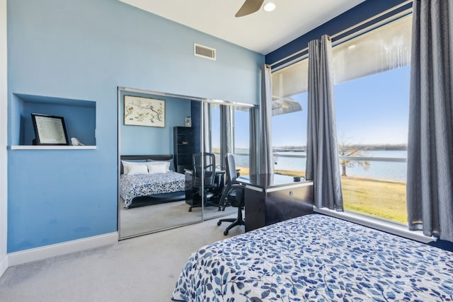 carpeted bedroom with ceiling fan, a water view, and a closet