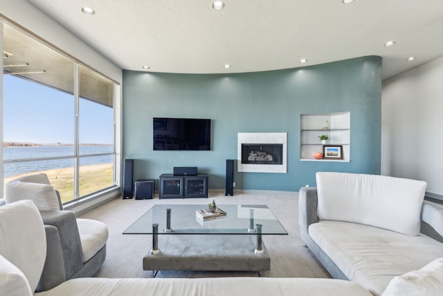 living room featuring a high end fireplace, a water view, light colored carpet, and a textured ceiling