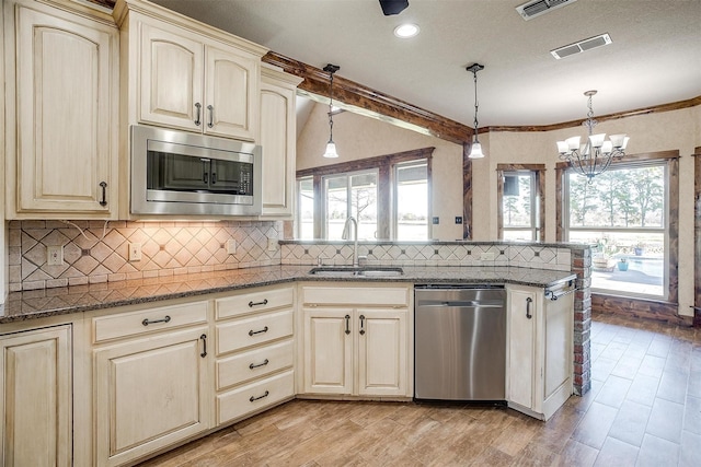 kitchen with sink, hanging light fixtures, dark stone countertops, a notable chandelier, and stainless steel appliances