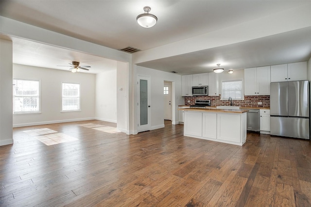 kitchen featuring white cabinets, decorative backsplash, ceiling fan, wood-type flooring, and stainless steel appliances