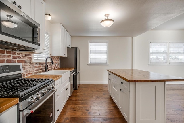 kitchen featuring appliances with stainless steel finishes, dark wood-type flooring, sink, white cabinets, and butcher block countertops