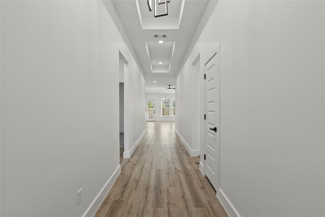 hall with a raised ceiling and light hardwood / wood-style flooring