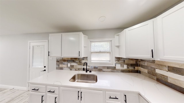 kitchen with light stone countertops, tasteful backsplash, white cabinetry, and sink