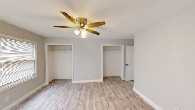 unfurnished bedroom featuring ceiling fan, light wood-type flooring, and two closets