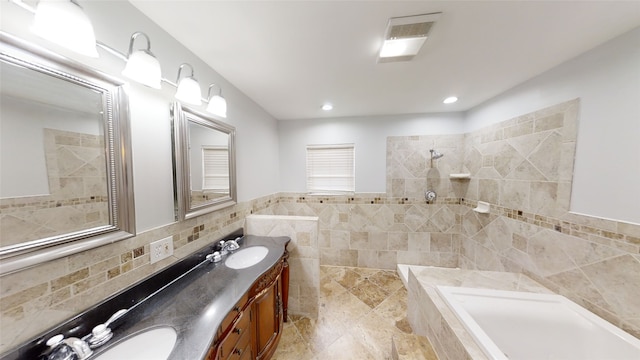 bathroom featuring tiled tub, vanity, and tile walls