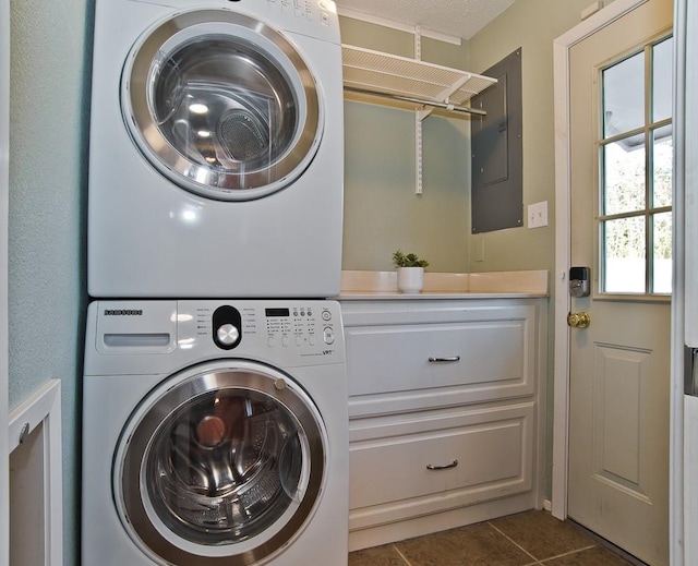 laundry area featuring dark tile patterned floors, stacked washing maching and dryer, and electric panel