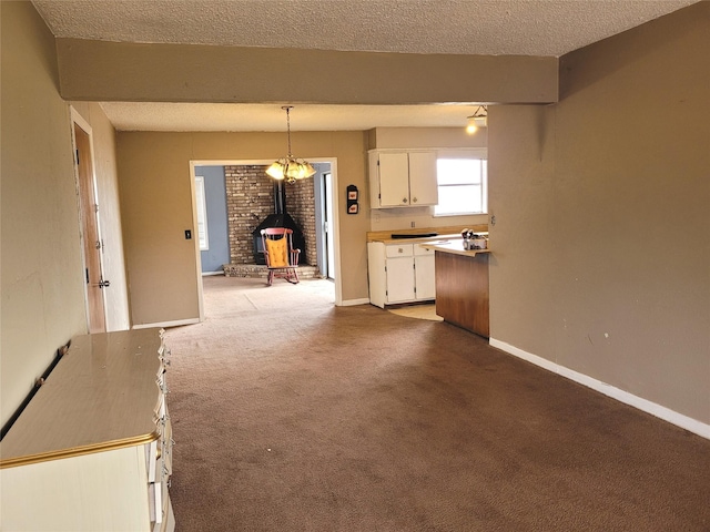 kitchen with a wood stove, light colored carpet, a textured ceiling, decorative light fixtures, and white cabinets