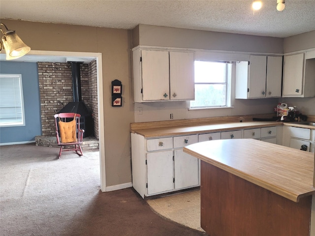 kitchen with light carpet, a textured ceiling, white cabinetry, and a wood stove