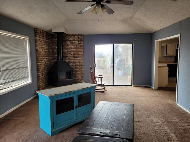 unfurnished living room featuring a wood stove, vaulted ceiling, ceiling fan, a textured ceiling, and carpet floors