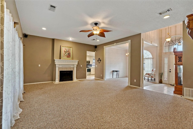 unfurnished living room featuring ceiling fan, light colored carpet, a tile fireplace, and a textured ceiling