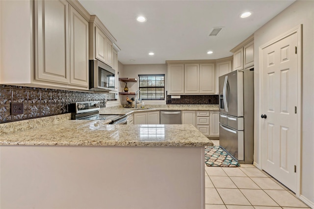 kitchen featuring sink, light stone counters, light tile patterned floors, appliances with stainless steel finishes, and kitchen peninsula