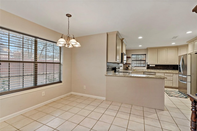 kitchen featuring pendant lighting, appliances with stainless steel finishes, light stone counters, tasteful backsplash, and kitchen peninsula