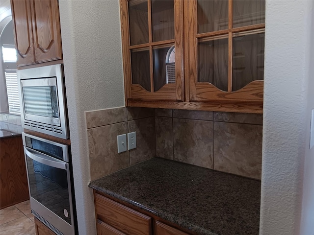 kitchen with dark stone countertops, stainless steel appliances, light tile patterned floors, and backsplash