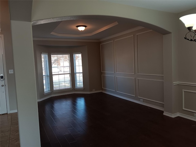 empty room with crown molding, dark hardwood / wood-style floors, and a raised ceiling